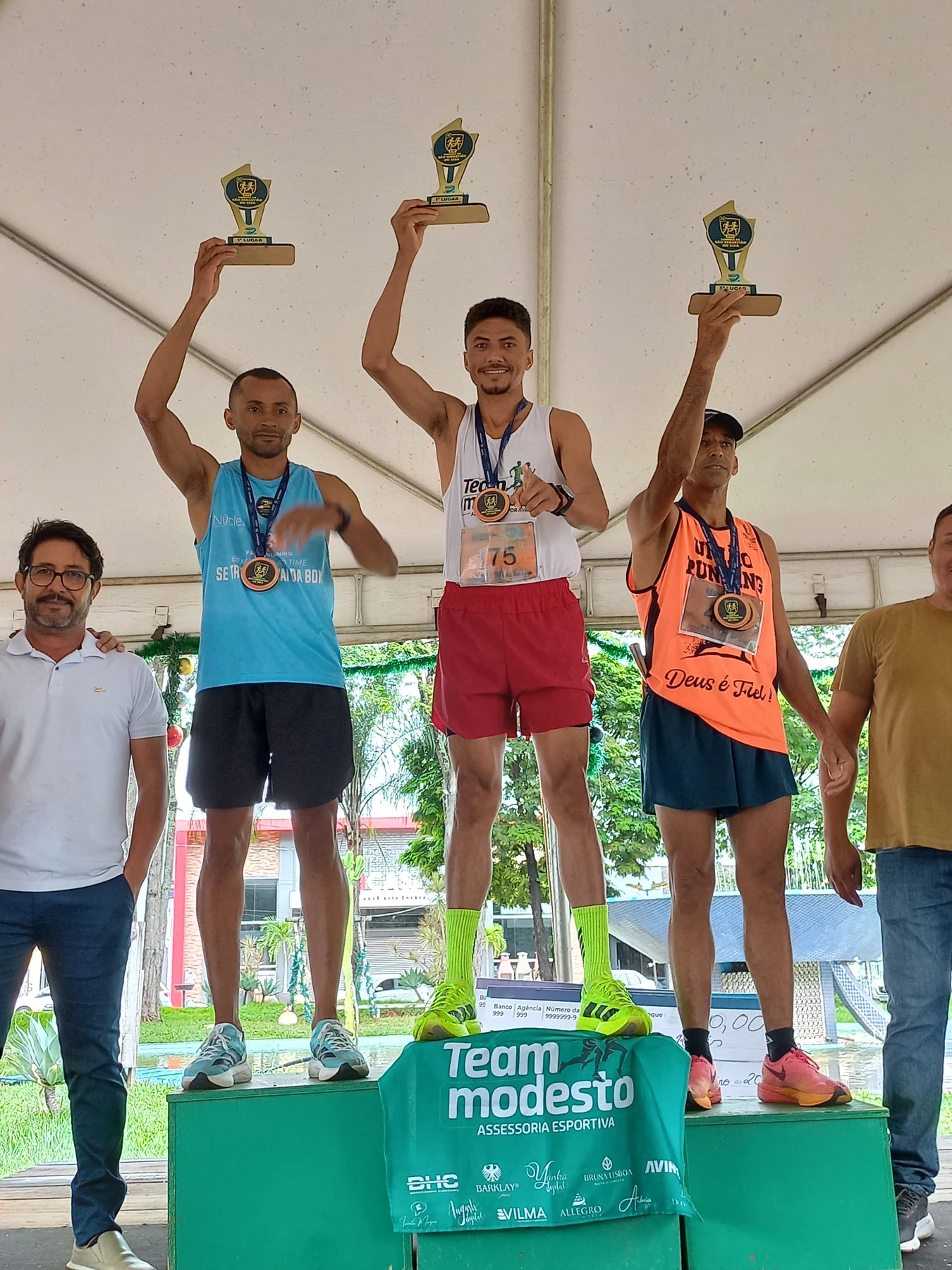Landim no centro do pódio, erguendo seu troféu acima da cabeça, ao lado dos demais atletas.