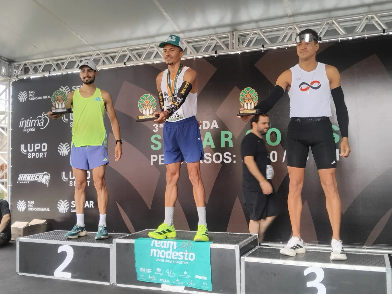 Landim de boné verde e troféu nas mãos, no centro do pódio, ao lado dos demais premiados.